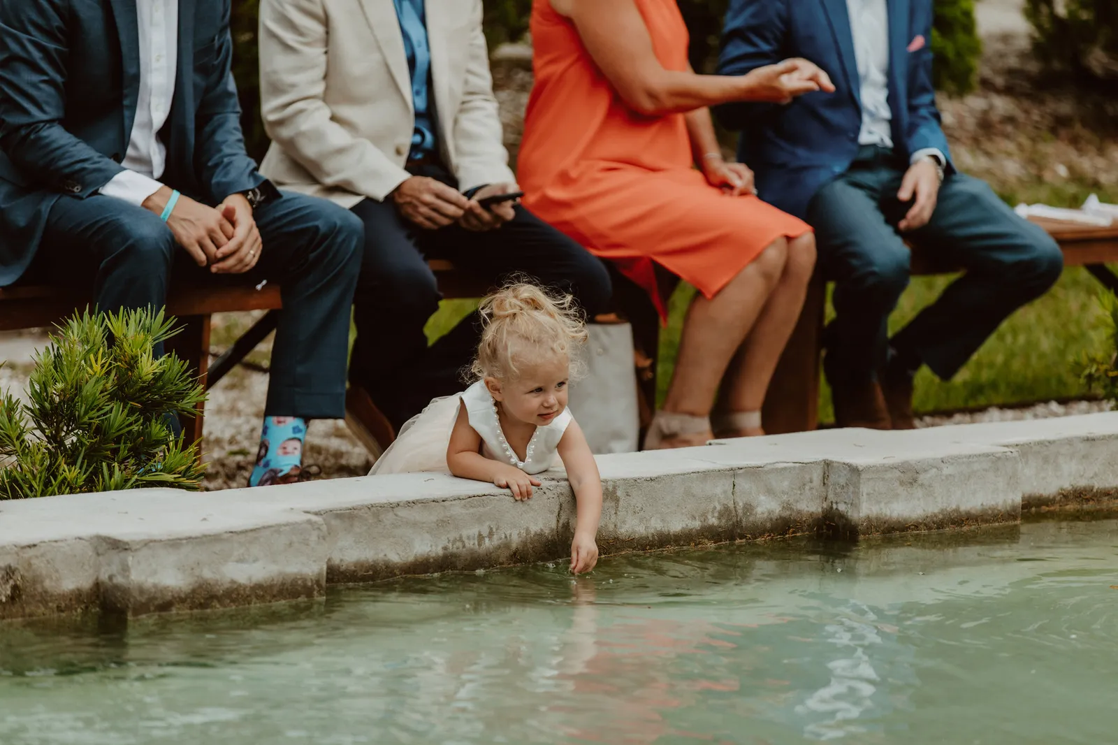 Toddler reaching into a pond beside seated guests