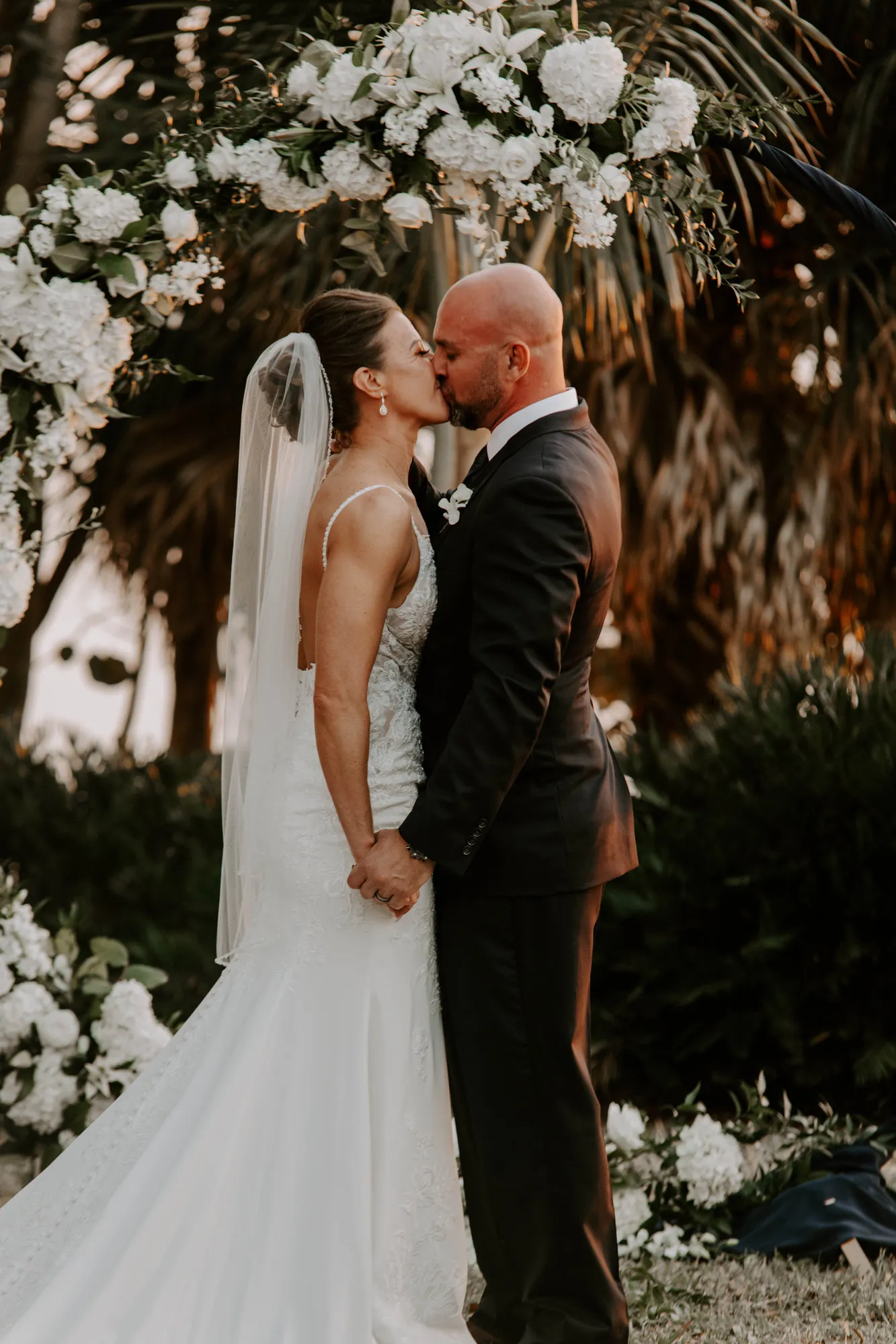 Bride and groom kissing at their sunset ceremony beneath a floral arch