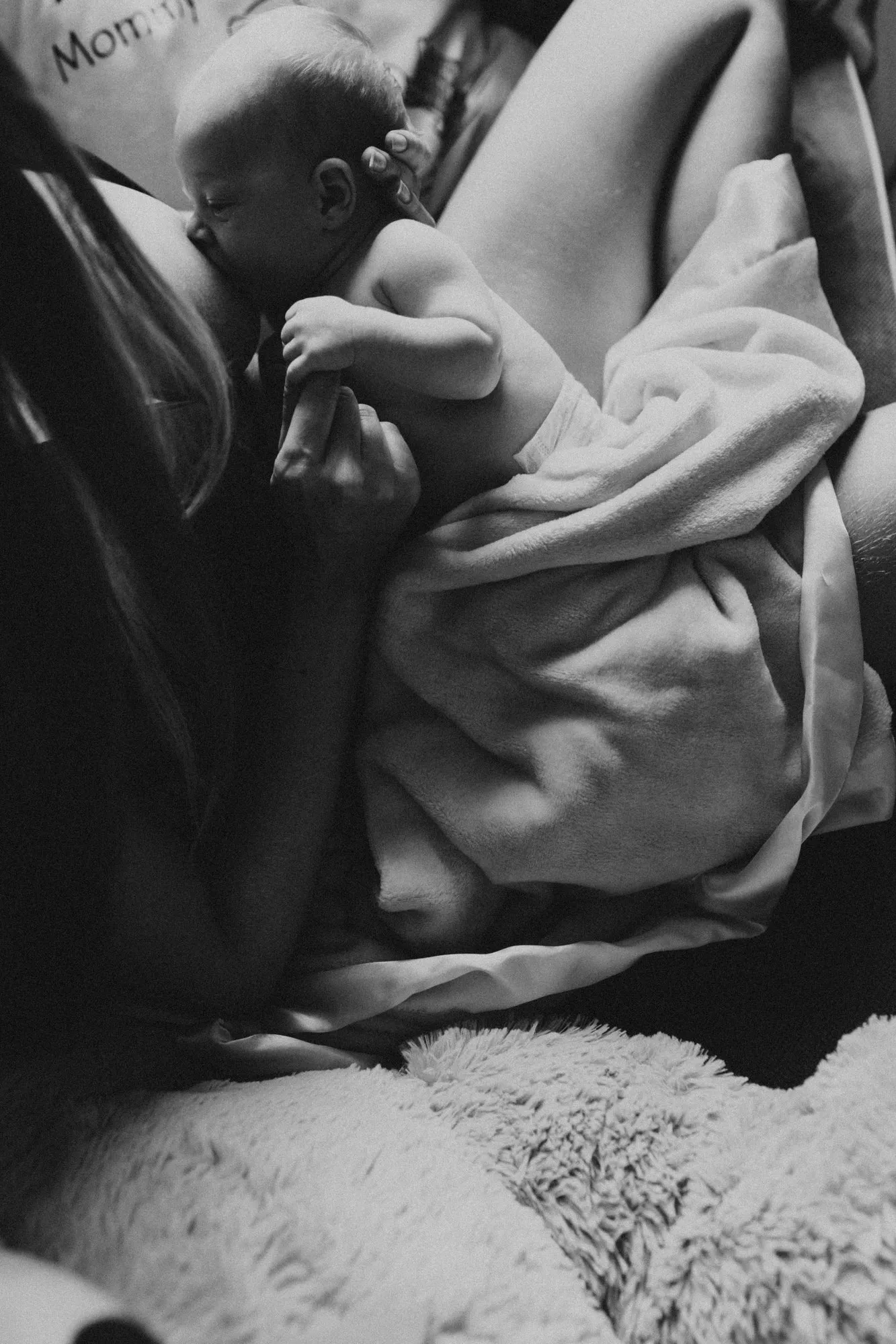 Newborn nursing under a soft blanket, in black and white