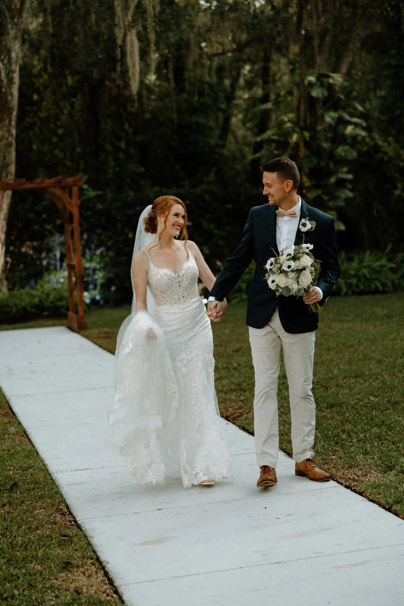 Bride and groom smiling at each other as they walk the path hand in hand