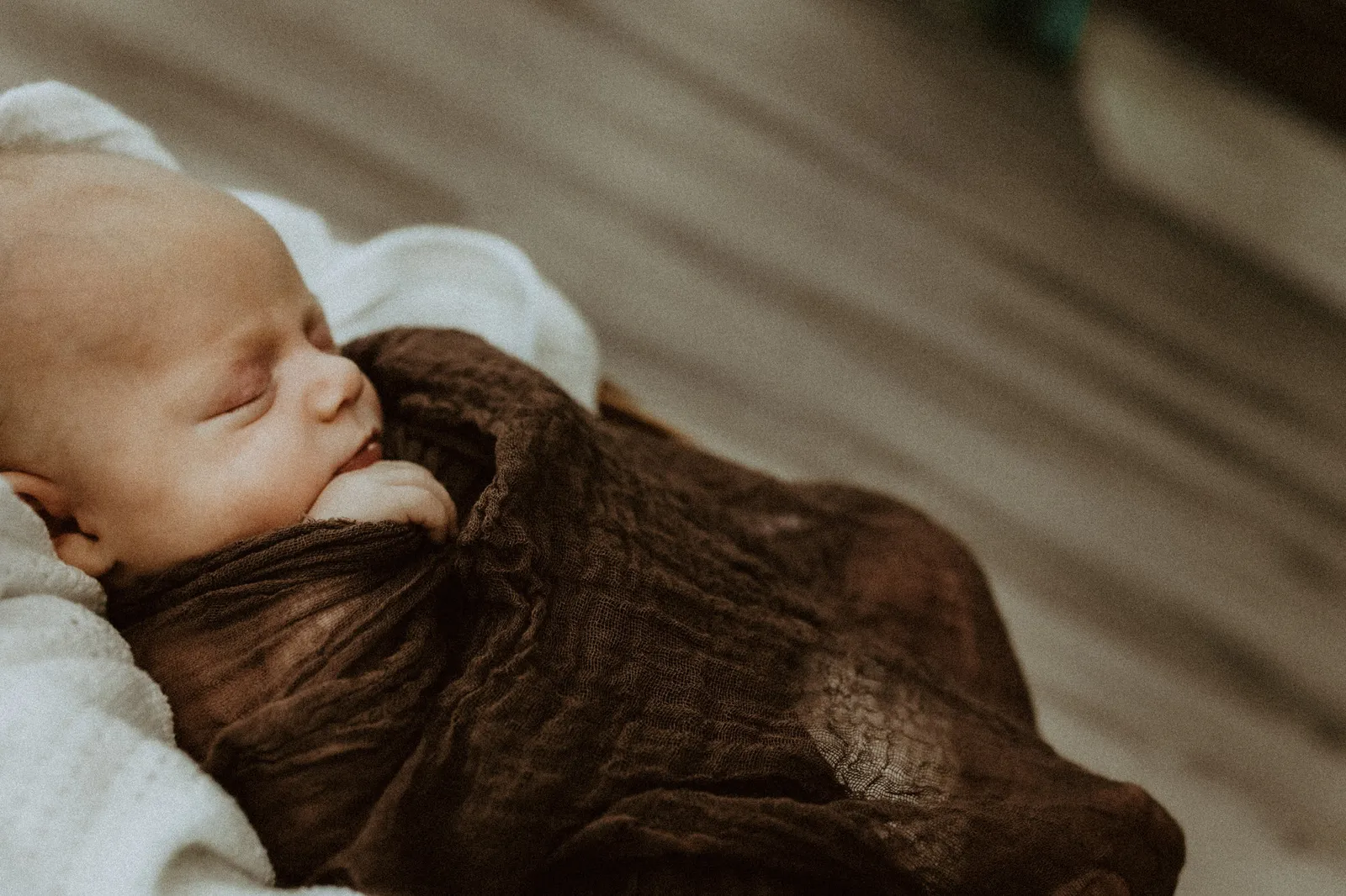 Sleeping newborn in brown muslin, seen in profile