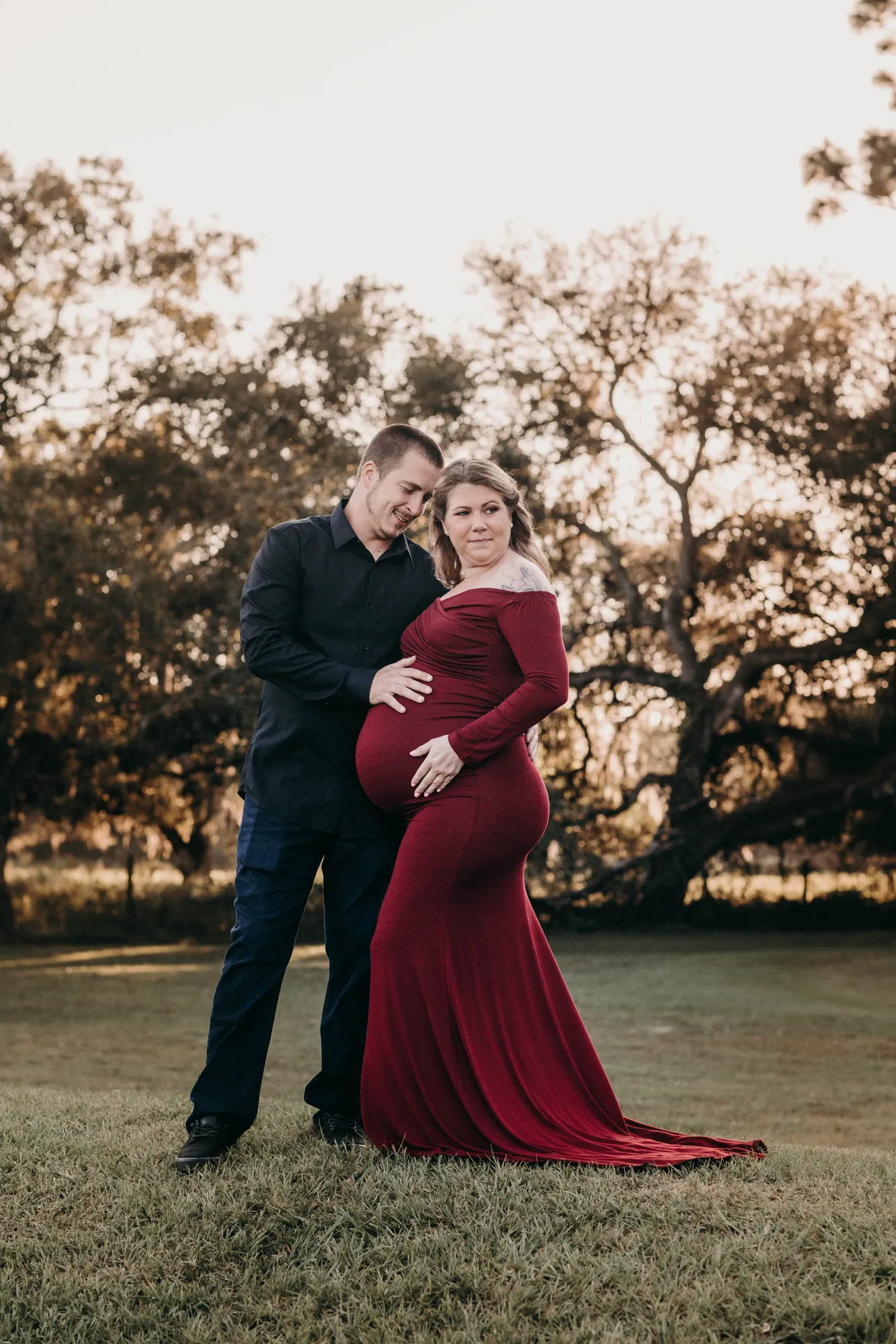 Couple in front of the oak, her red train spread on the grass