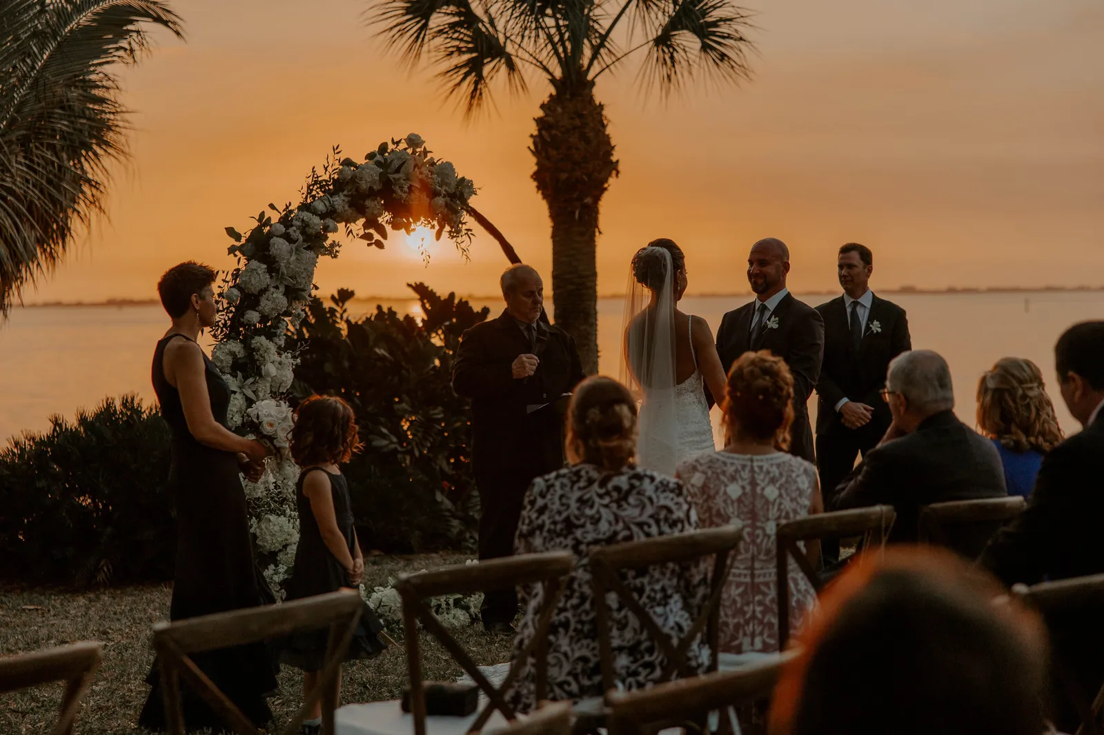 Ceremony under a circular floral arch as the sun sets over the bay