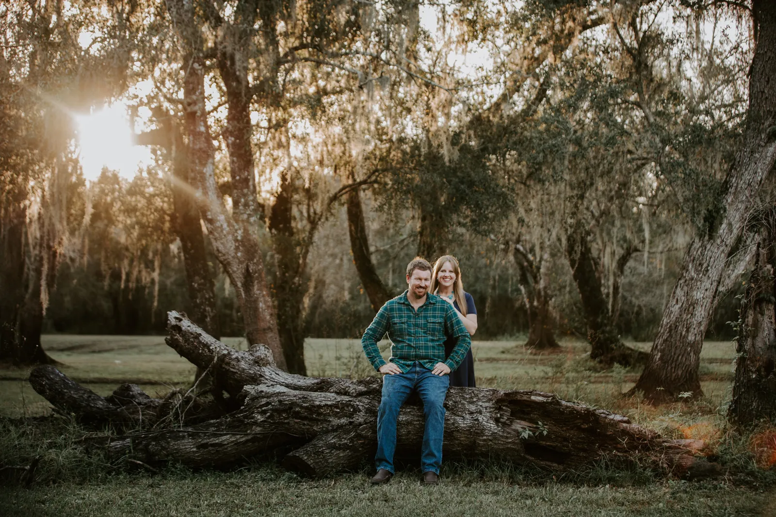 Couple at a fallen tree under moss-draped oaks, the sun low behind them