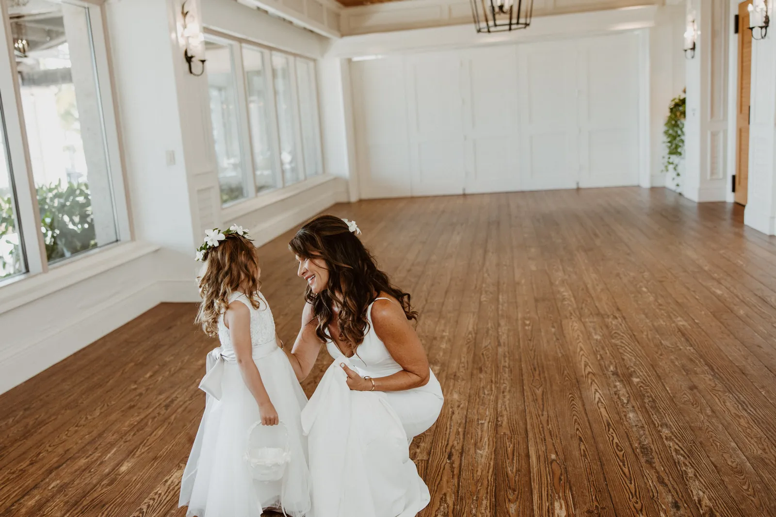 Bride bending down to talk with the flower girl in a sunlit room