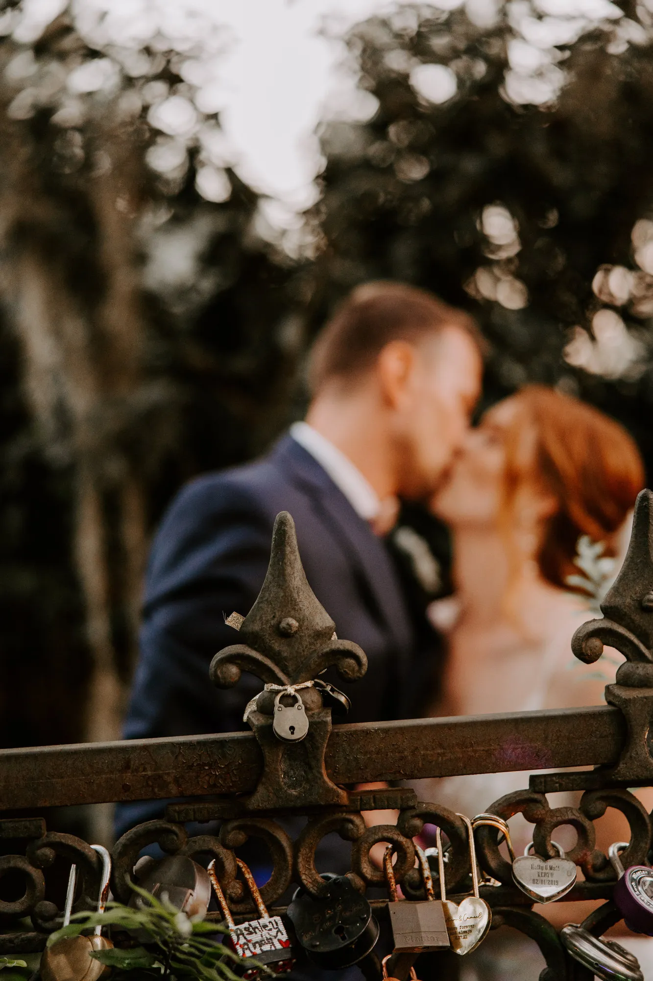 Bride and groom kissing behind an iron gate hung with padlocks