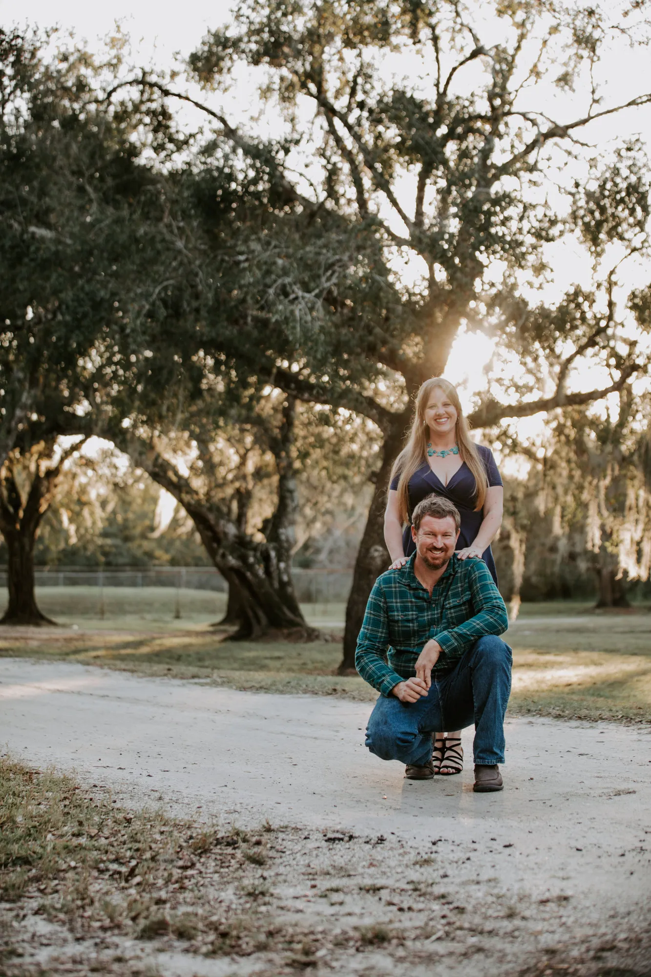 Man crouching on a dirt road with the woman standing behind him, hands on his shoulders