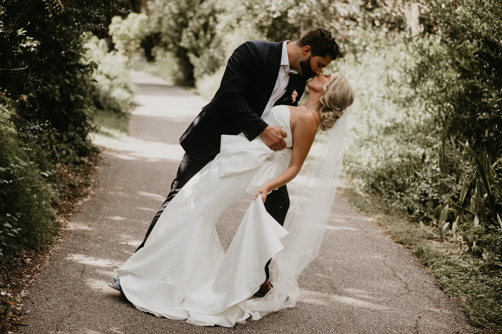 Groom dipping his bride for a kiss on a garden path