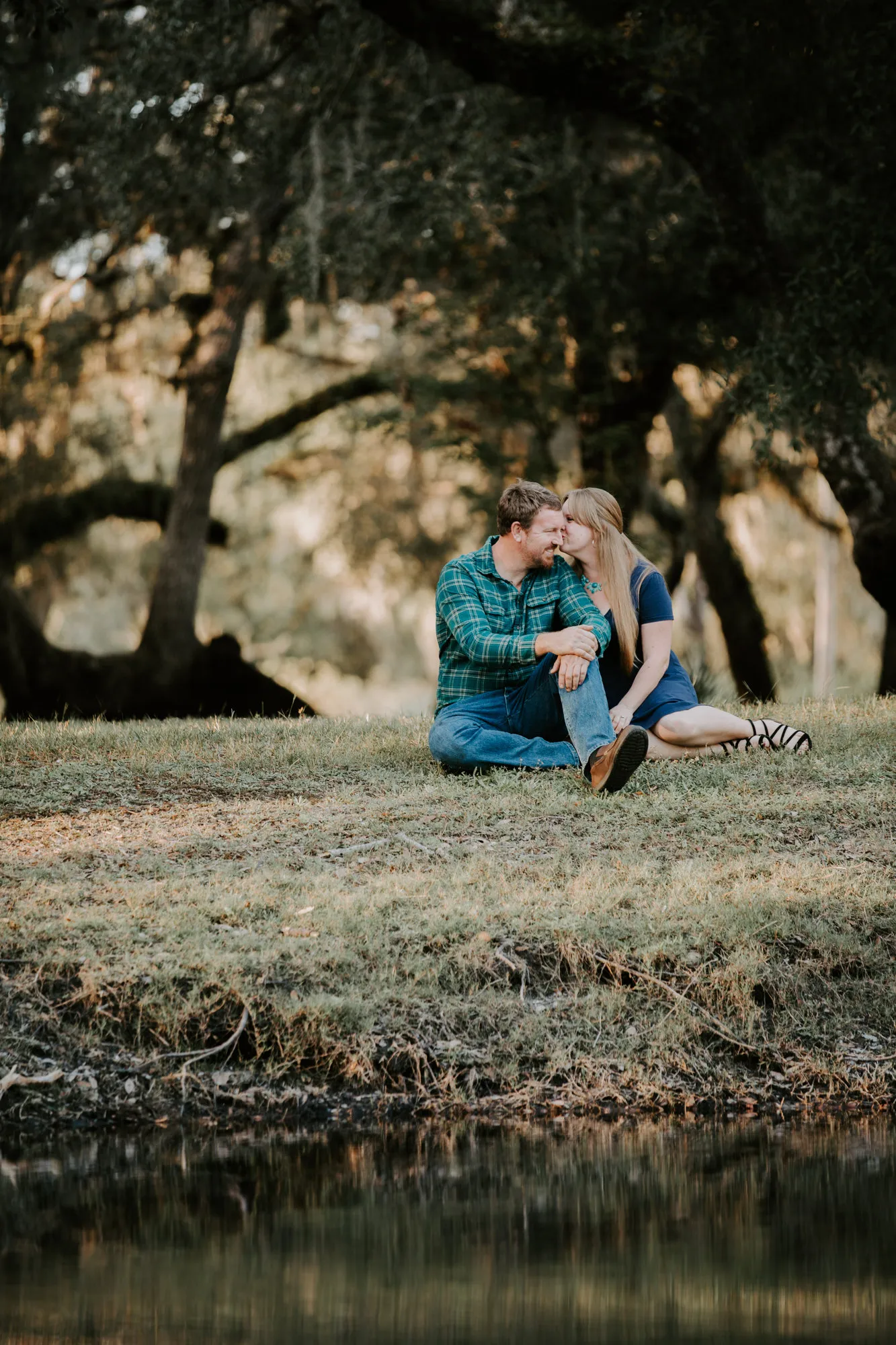 Couple sitting on the grass by a pond, foreheads together