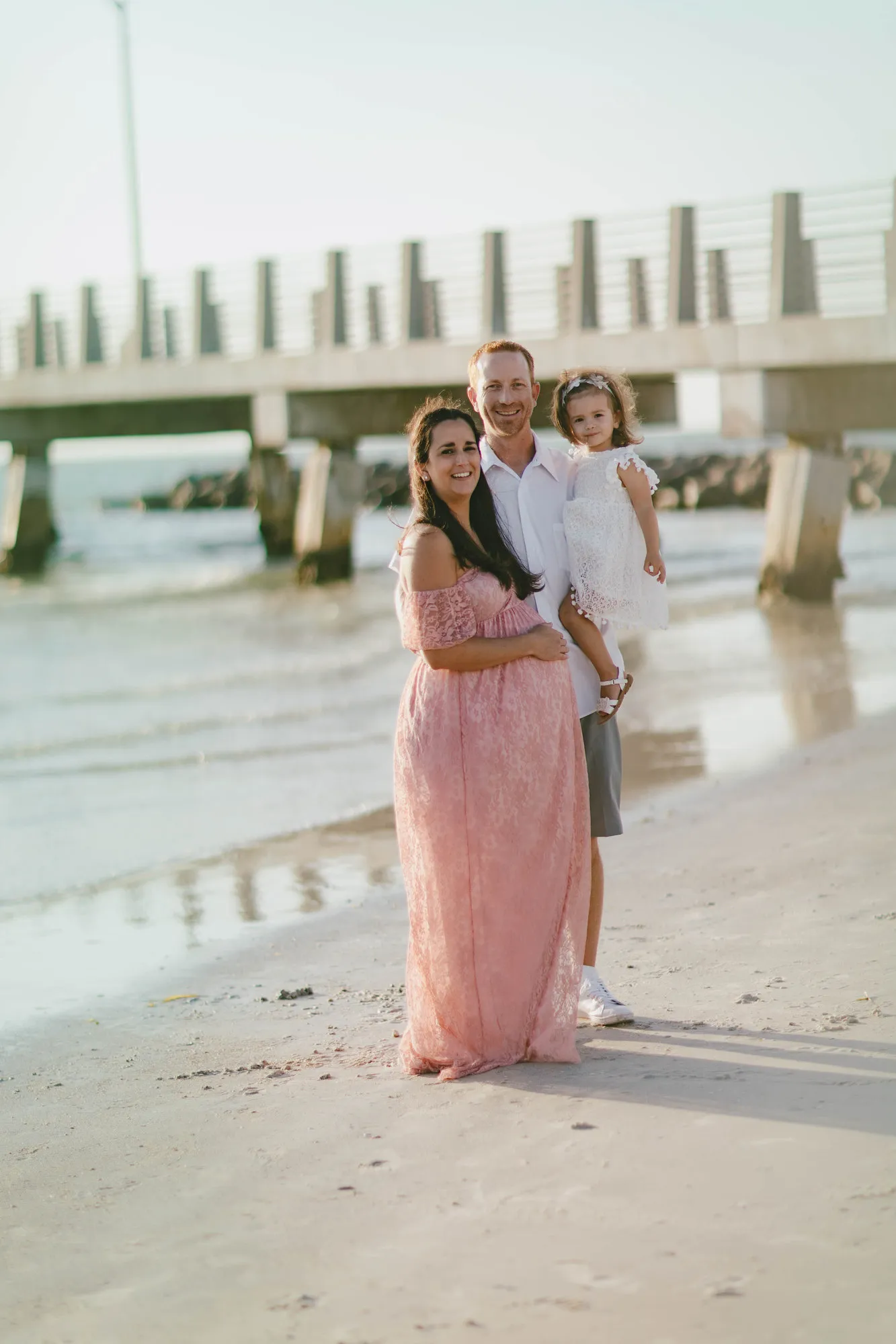 Family of three smiling for a portrait in front of the pier