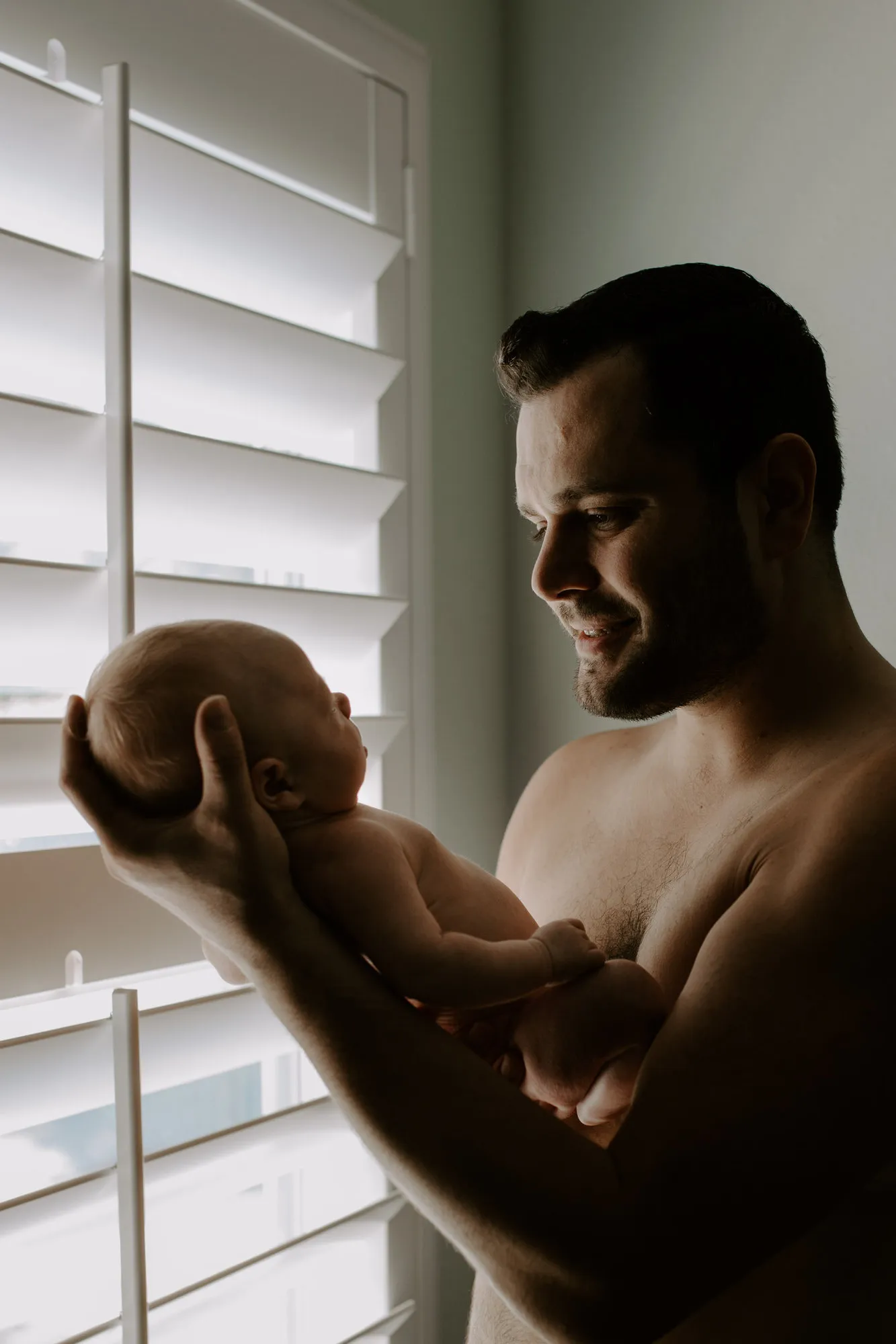 Father holding his newborn son beside a shuttered window