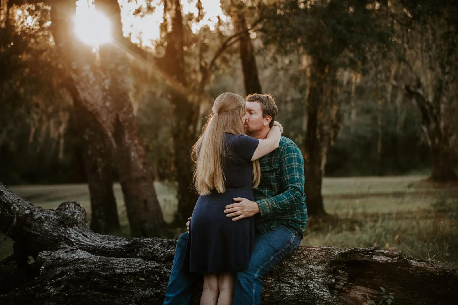 Couple embracing on a fallen tree as the sun sets through the oaks
