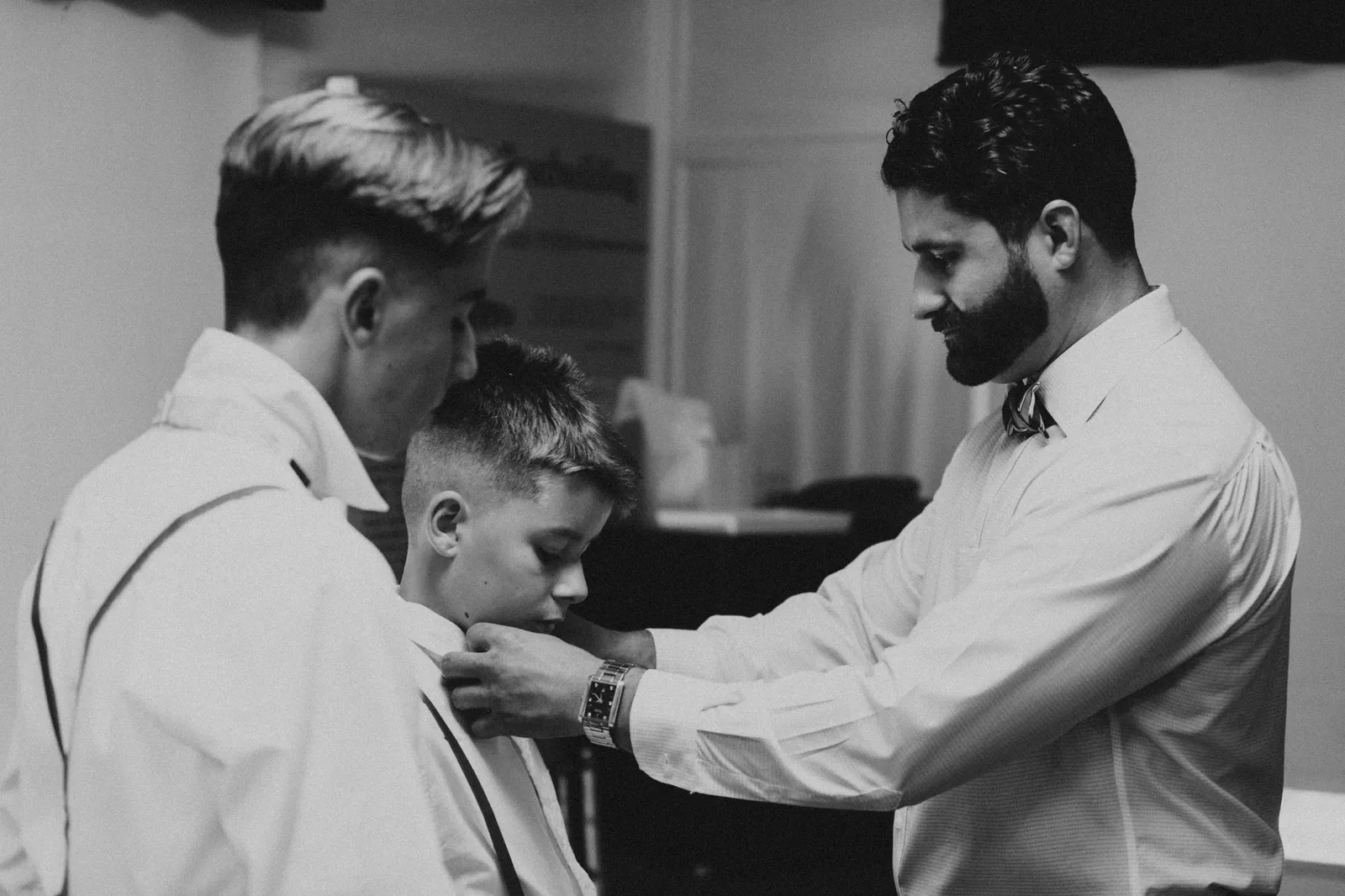 Groom adjusting a boy's bow tie, in black and white