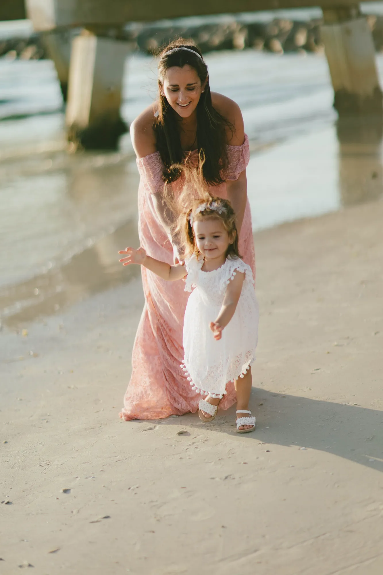 Mother bending to guide her toddler along the shoreline