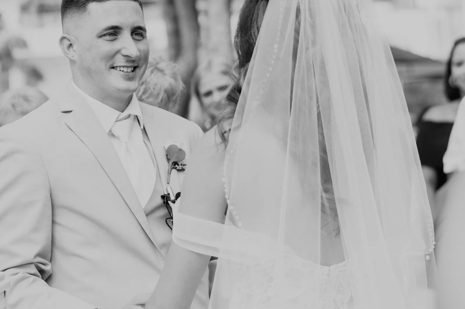 Groom smiling at his bride during the ceremony, in black and white