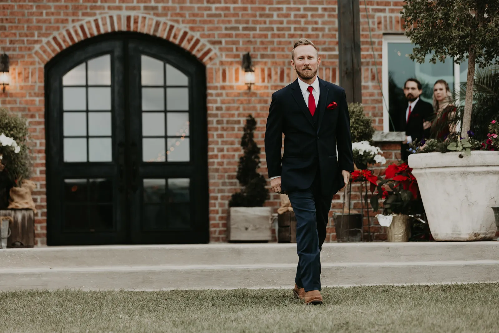 Groom walking across the lawn in front of a brick building