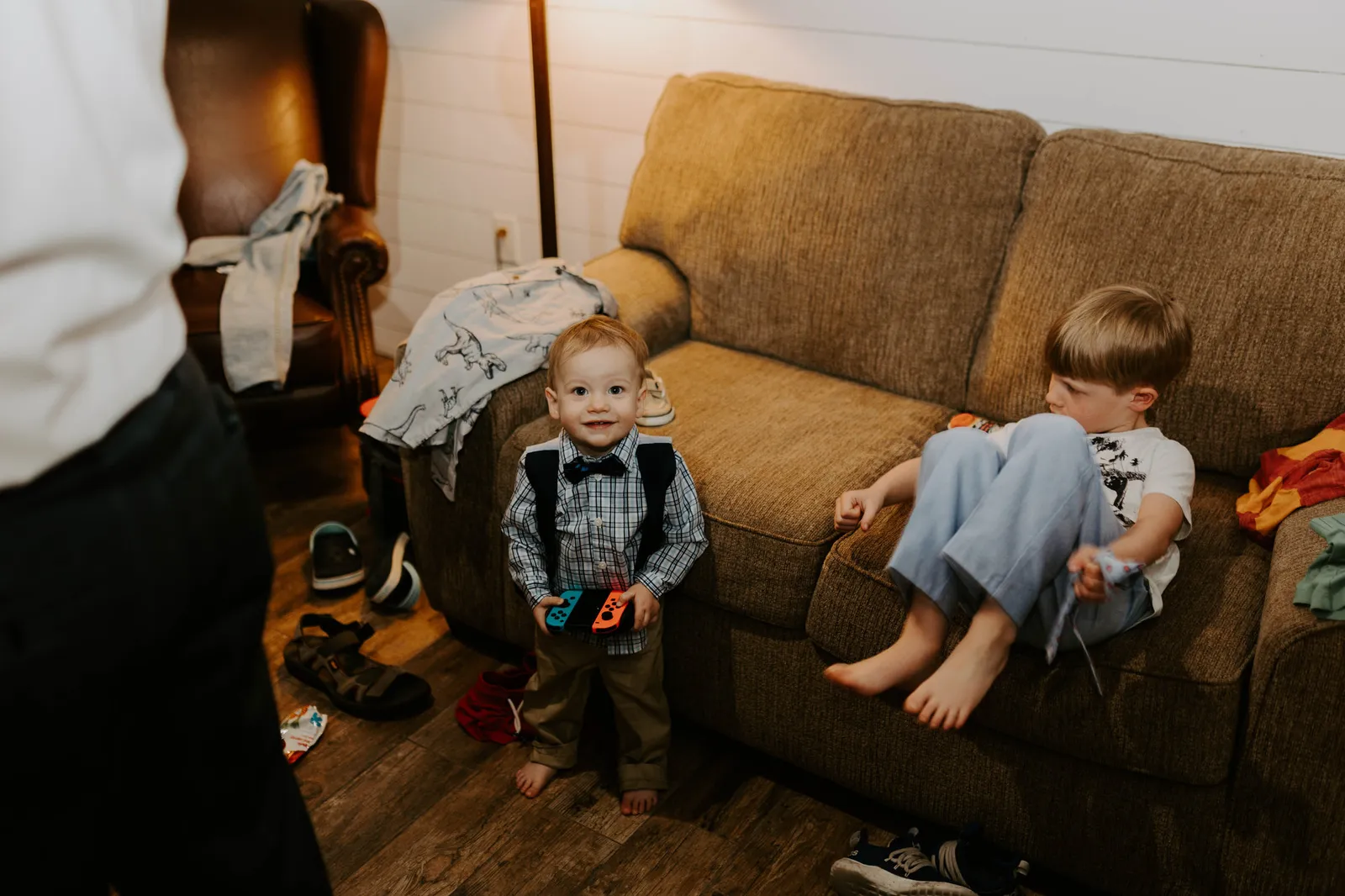 Two small boys beside a couch, one in suspenders and a bow tie