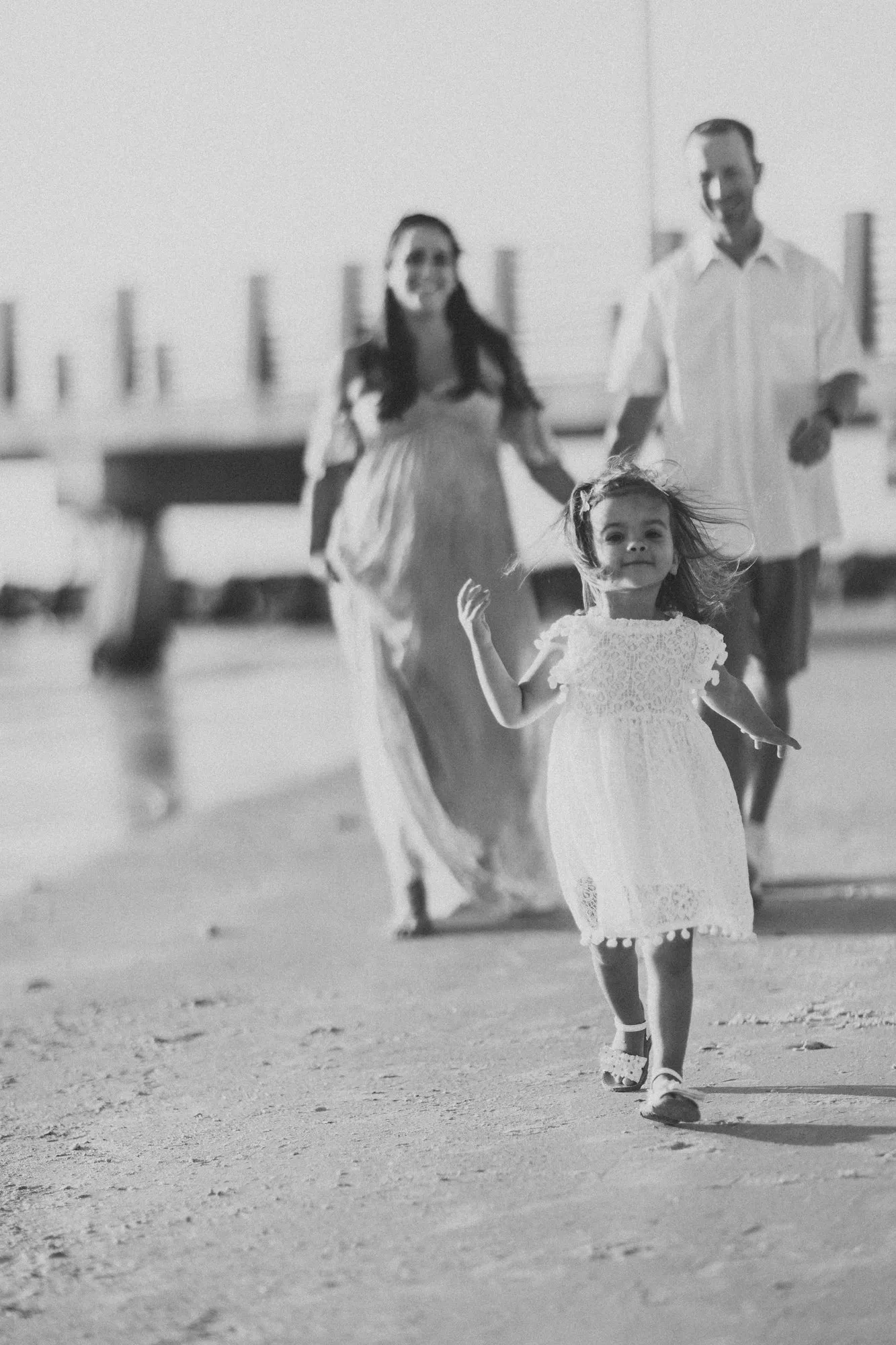 Toddler running ahead of her parents on the beach, in black and white