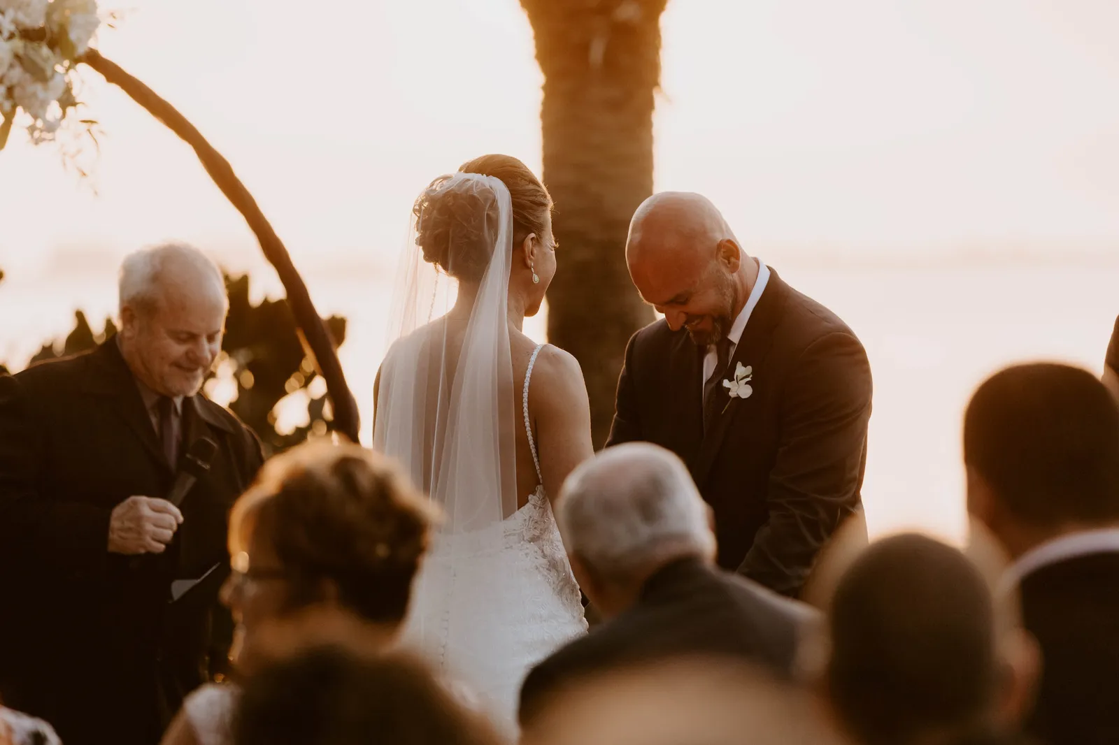 Groom bowing his head beside his bride during the ceremony at sunset