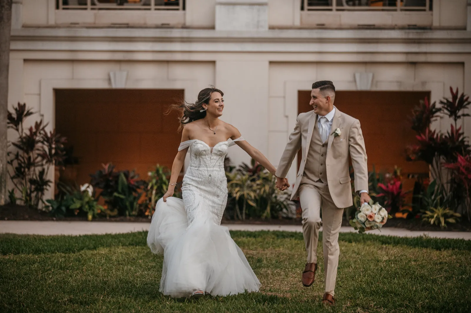 Bride and groom running hand in hand across the lawn