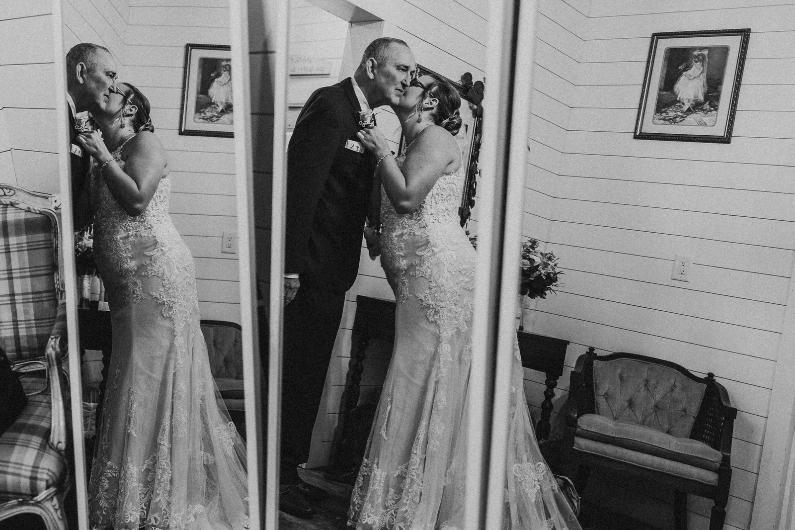 Man in a suit kissing the bride's cheek, reflected in two mirrors, in black and white