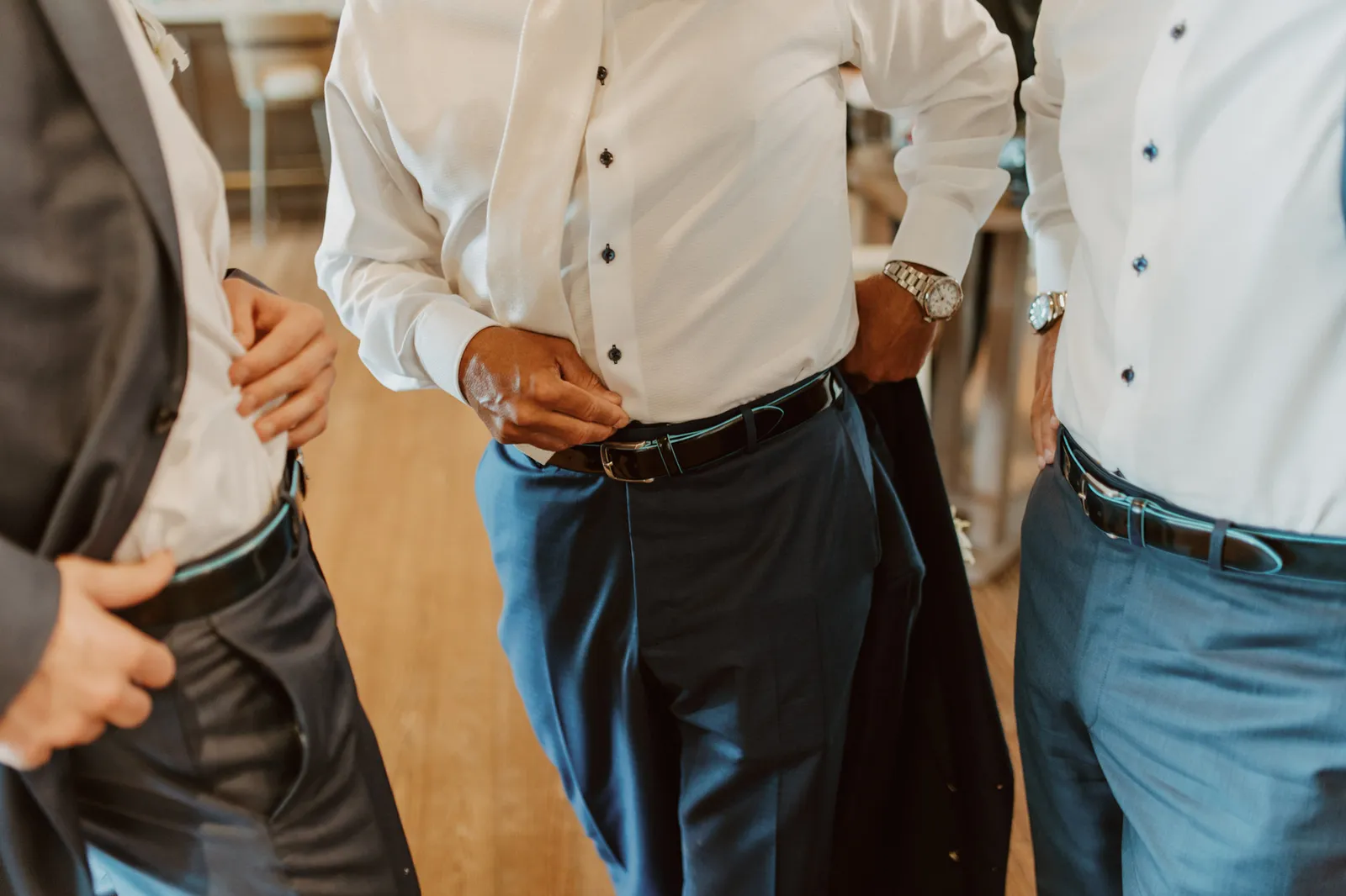 Close-up of three men in white shirts getting dressed