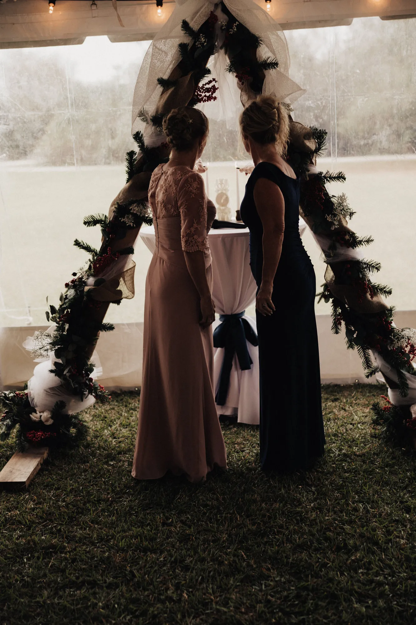 Two women silhouetted beneath a greenery-covered arch