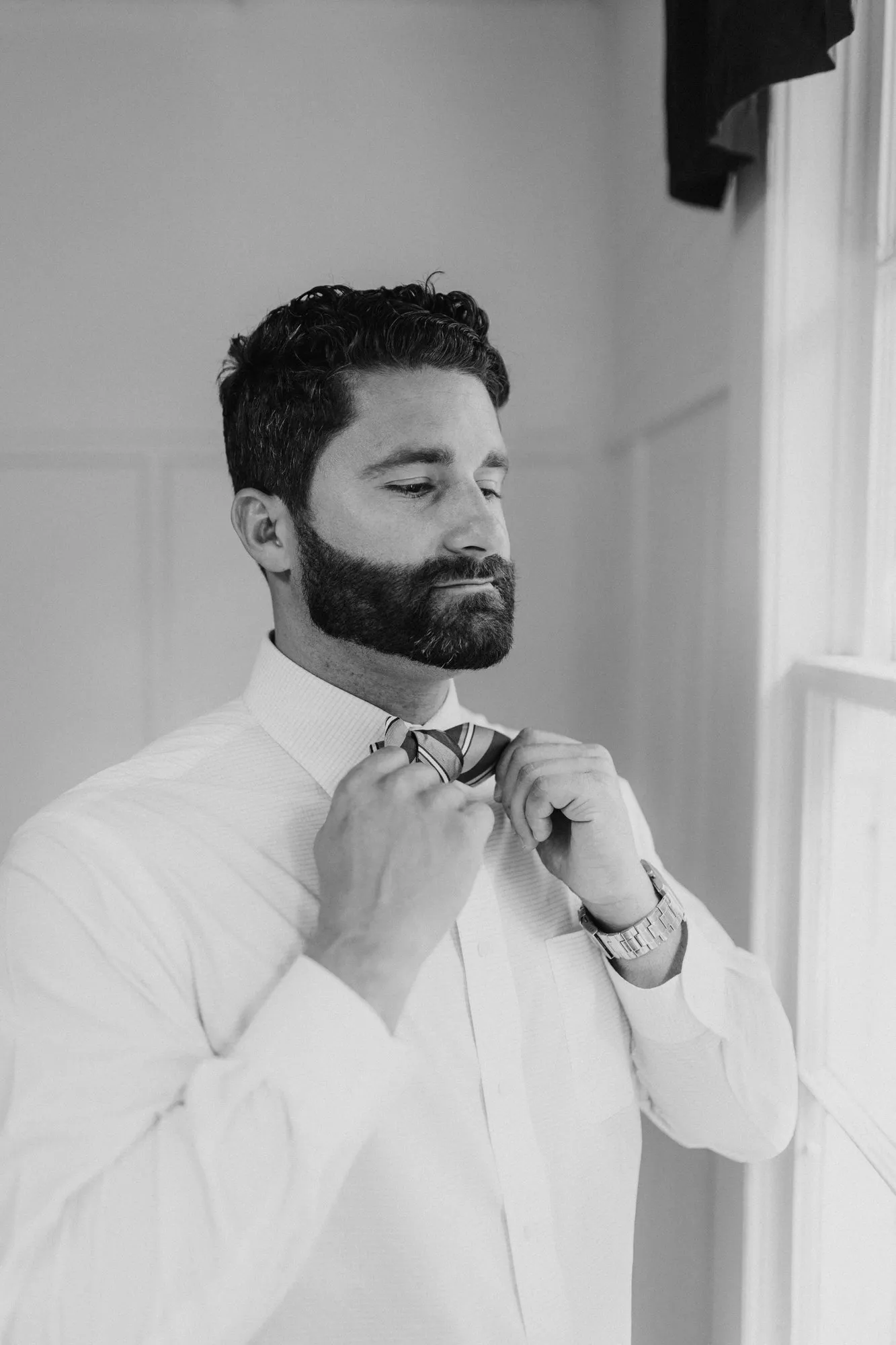 Groom with his eyes closed adjusting his bow tie, in black and white