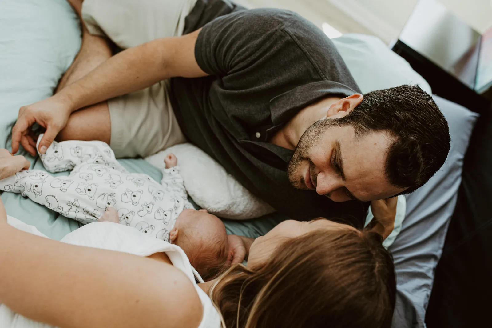 Father lying on the bed beside the newborn as the mother watches
