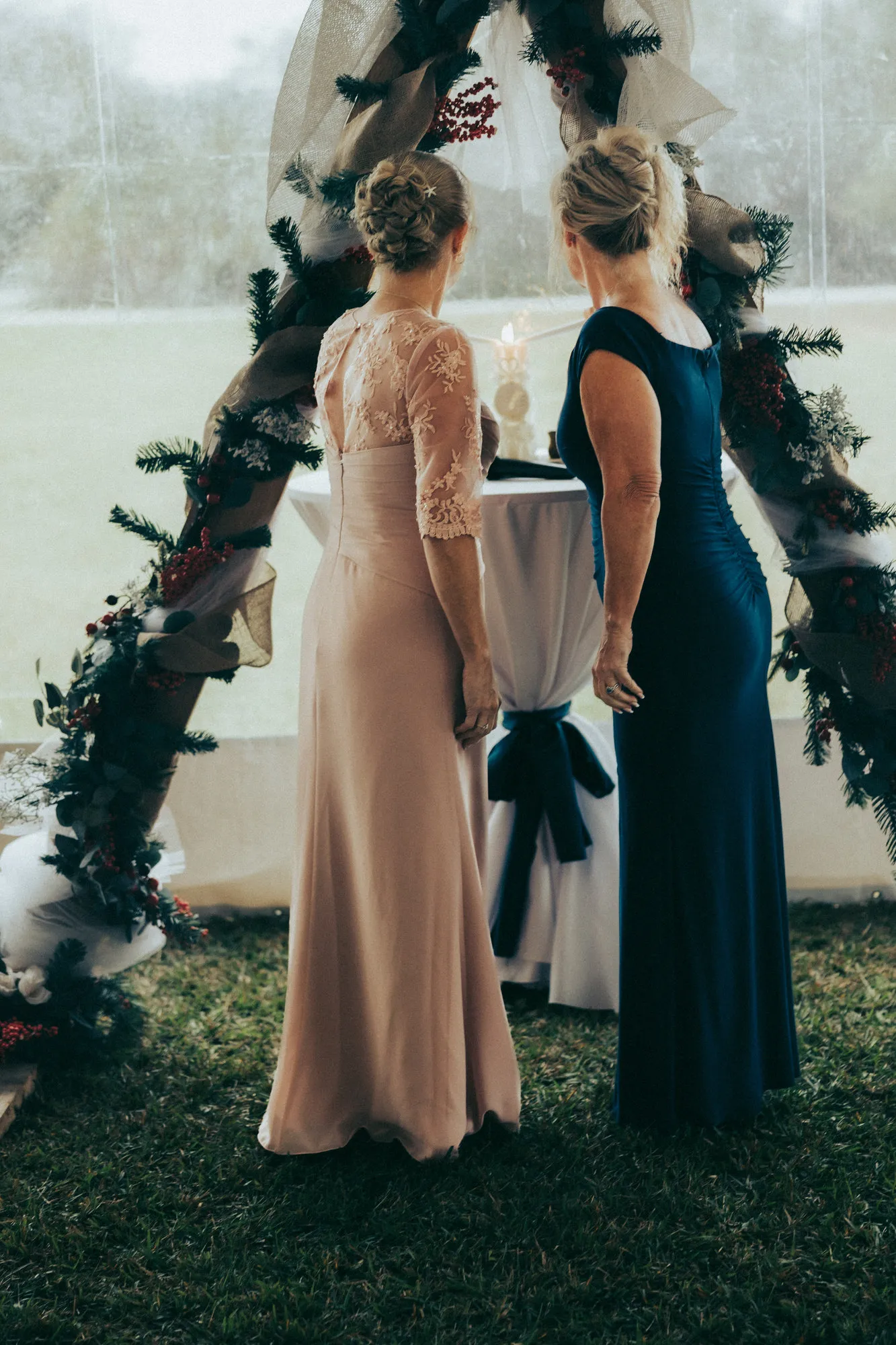 Two women in blush and navy dresses at a small table under the arch, seen from behind