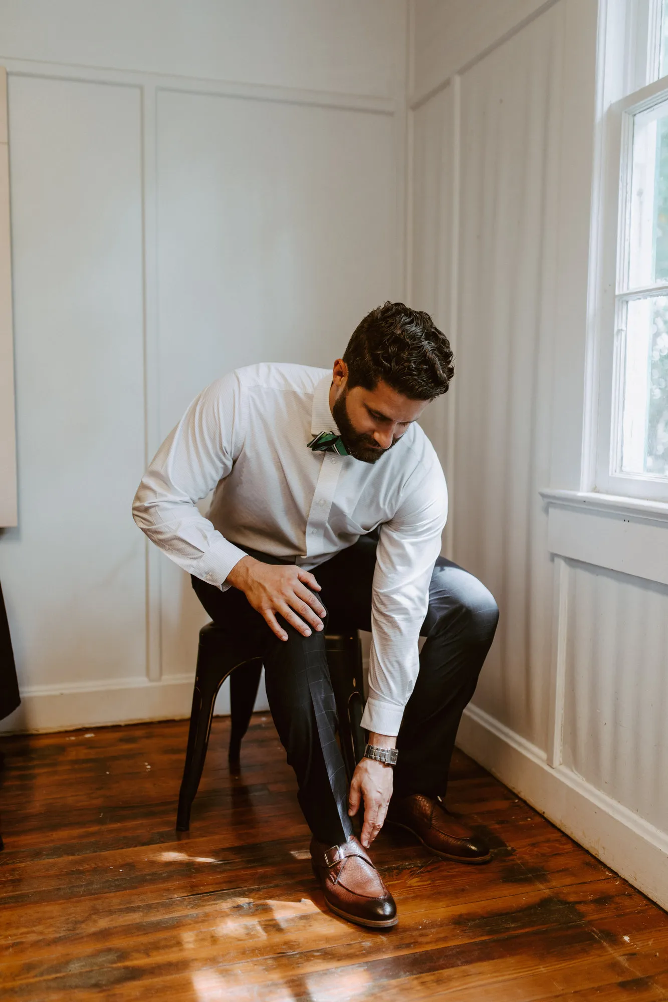 Groom tying his brown leather shoe beside a window