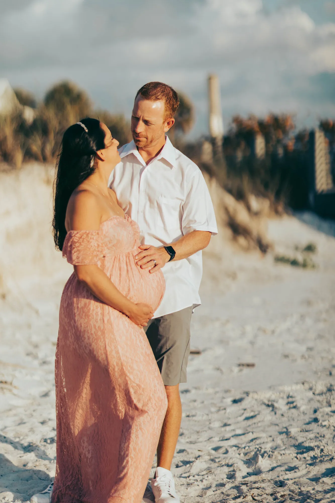 Couple laughing together among the dunes, her hands on her bump
