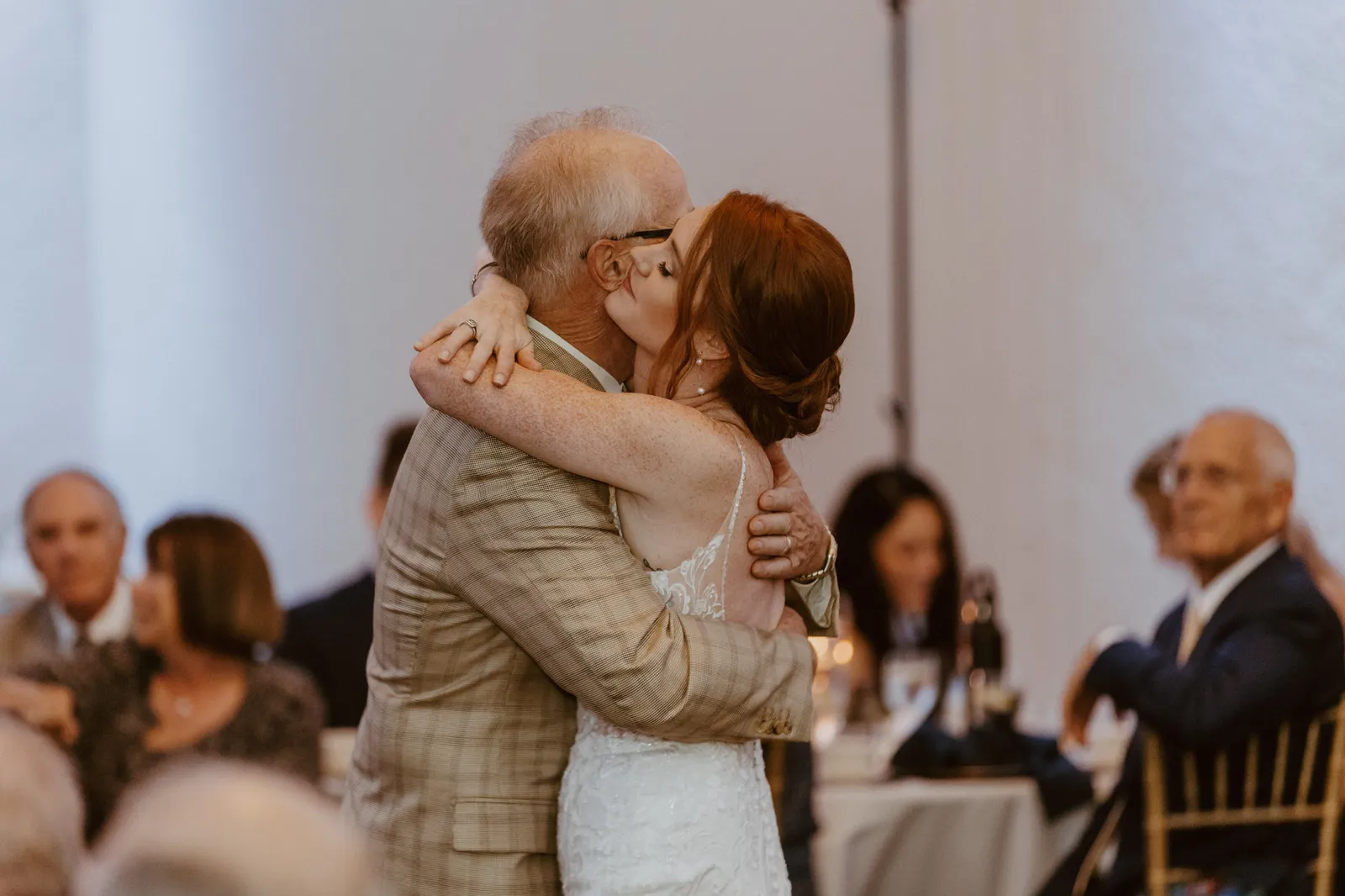 Bride hugging an older man in a plaid jacket at the reception