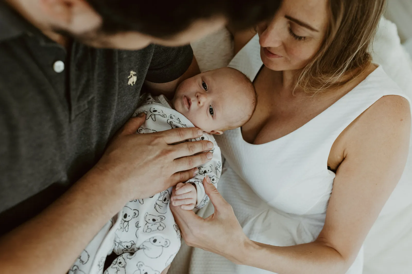 Newborn held between his parents, the father's hand on his chest