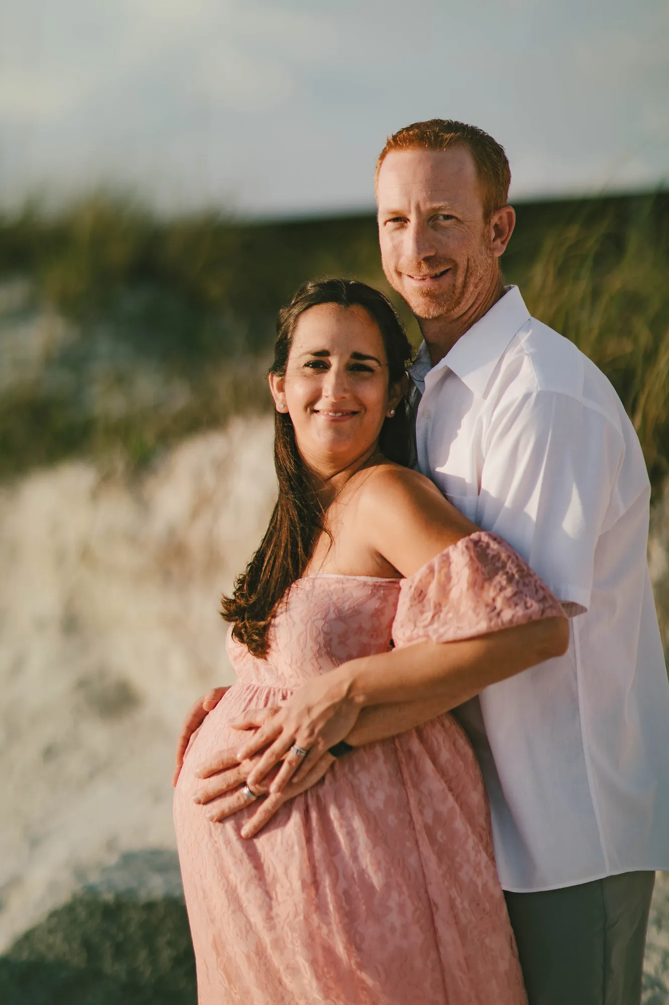 Husband standing behind his wife with his arms around her bump