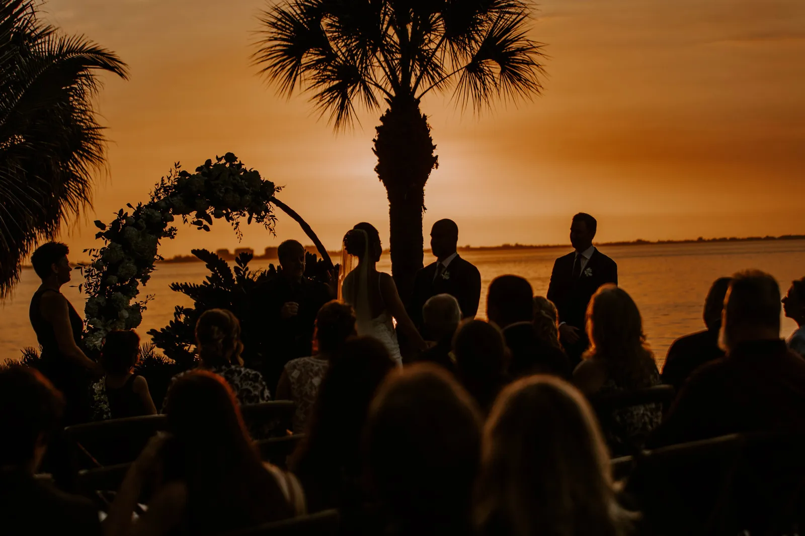 Wedding ceremony silhouetted against an orange sunset over Sarasota Bay
