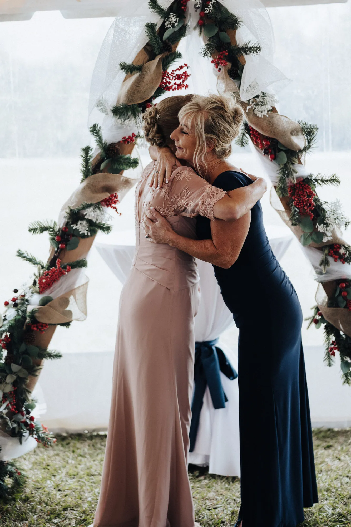 Two women hugging beneath a greenery-covered arch