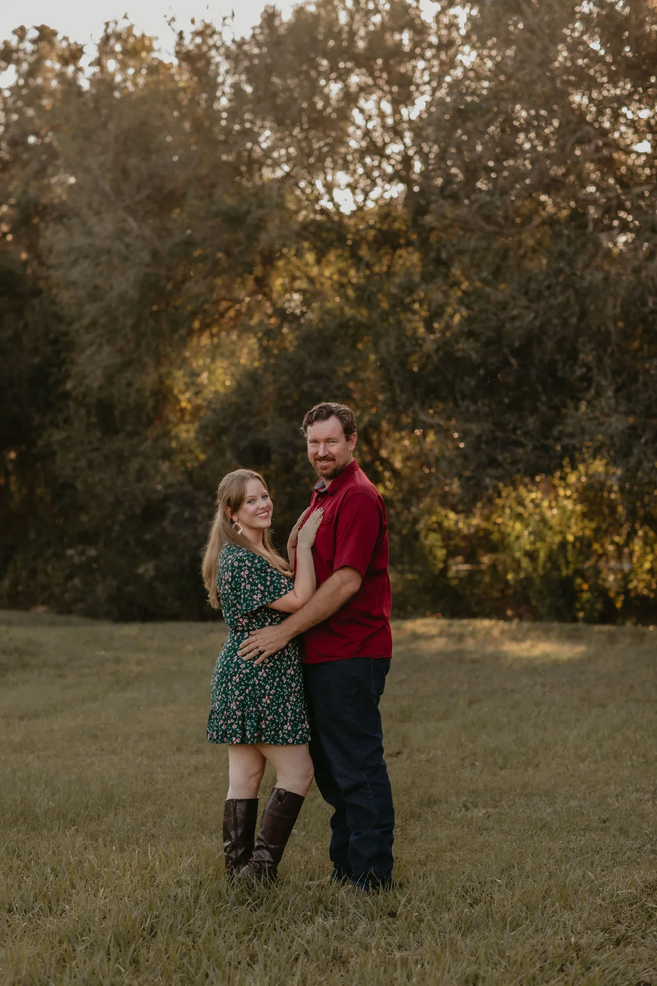 Couple standing together in a field at golden hour, her hand on his chest