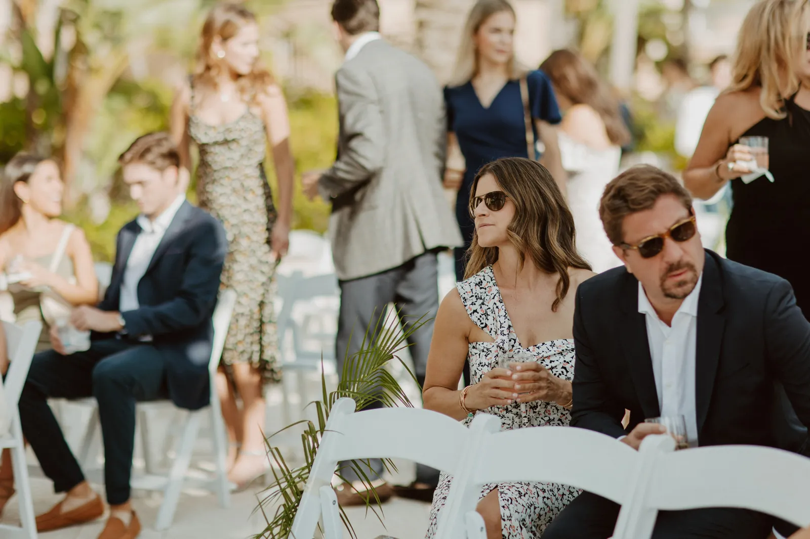 Guests in sunglasses seated on white chairs, waiting for the ceremony