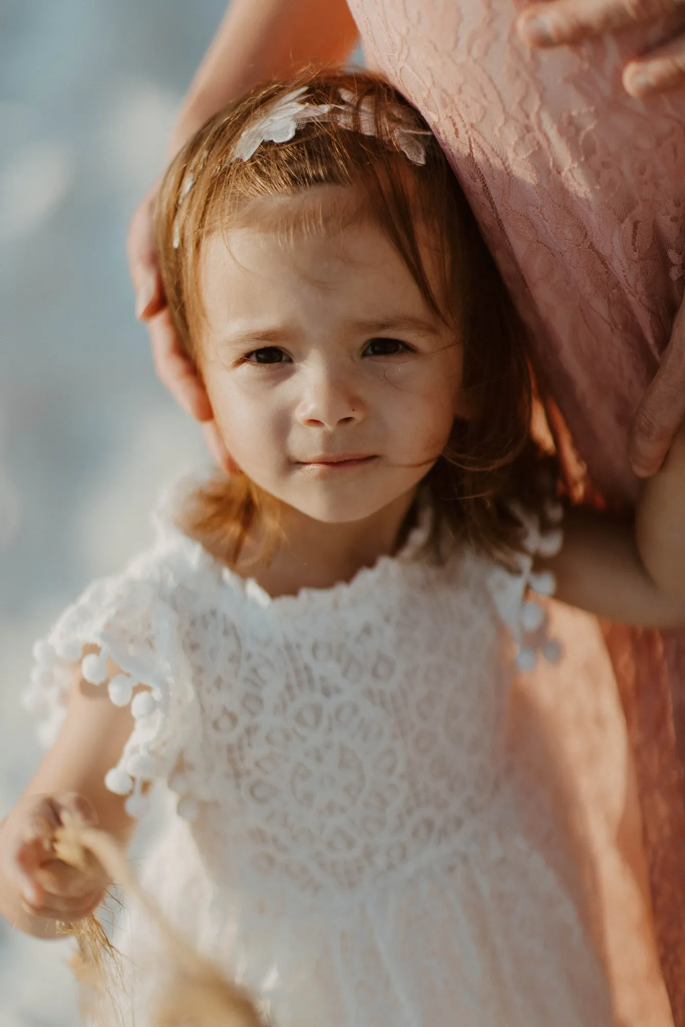 Toddler with a flower clip looking at the camera, holding her mother's hand
