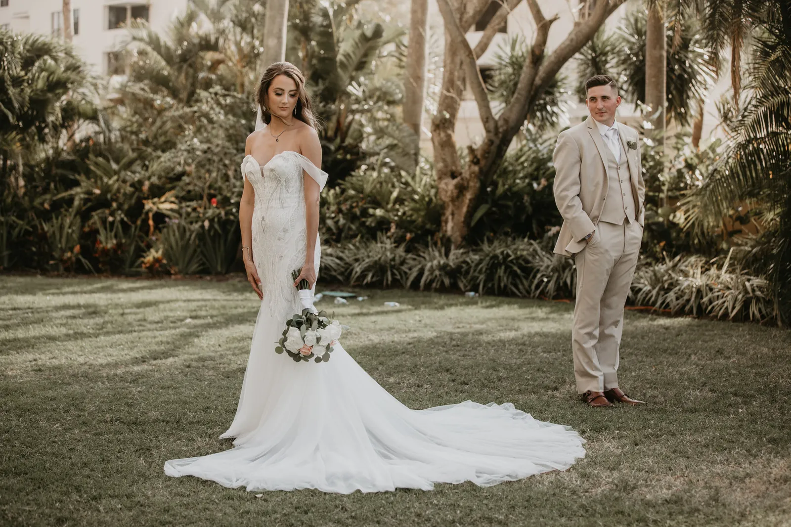 Bride looking down at her bouquet while the groom watches from behind her