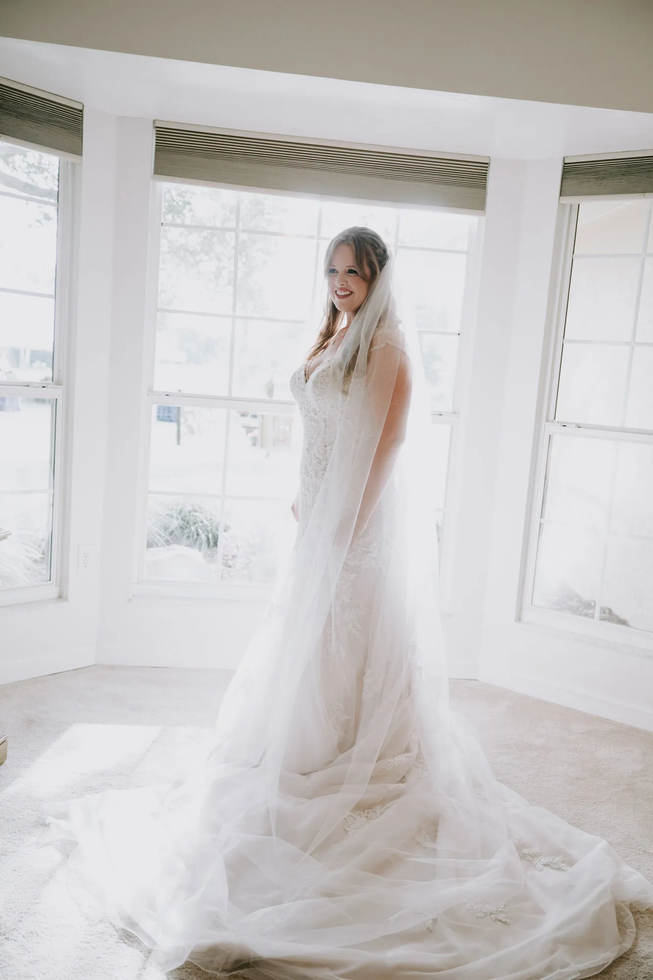 Bride in her gown and veil standing in a bay window