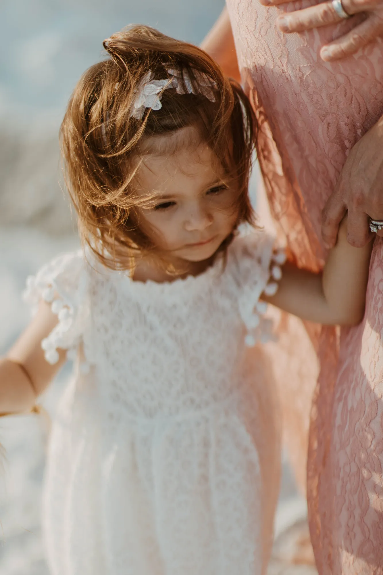 Toddler looking down, her hair blowing, beside her mother's pink gown