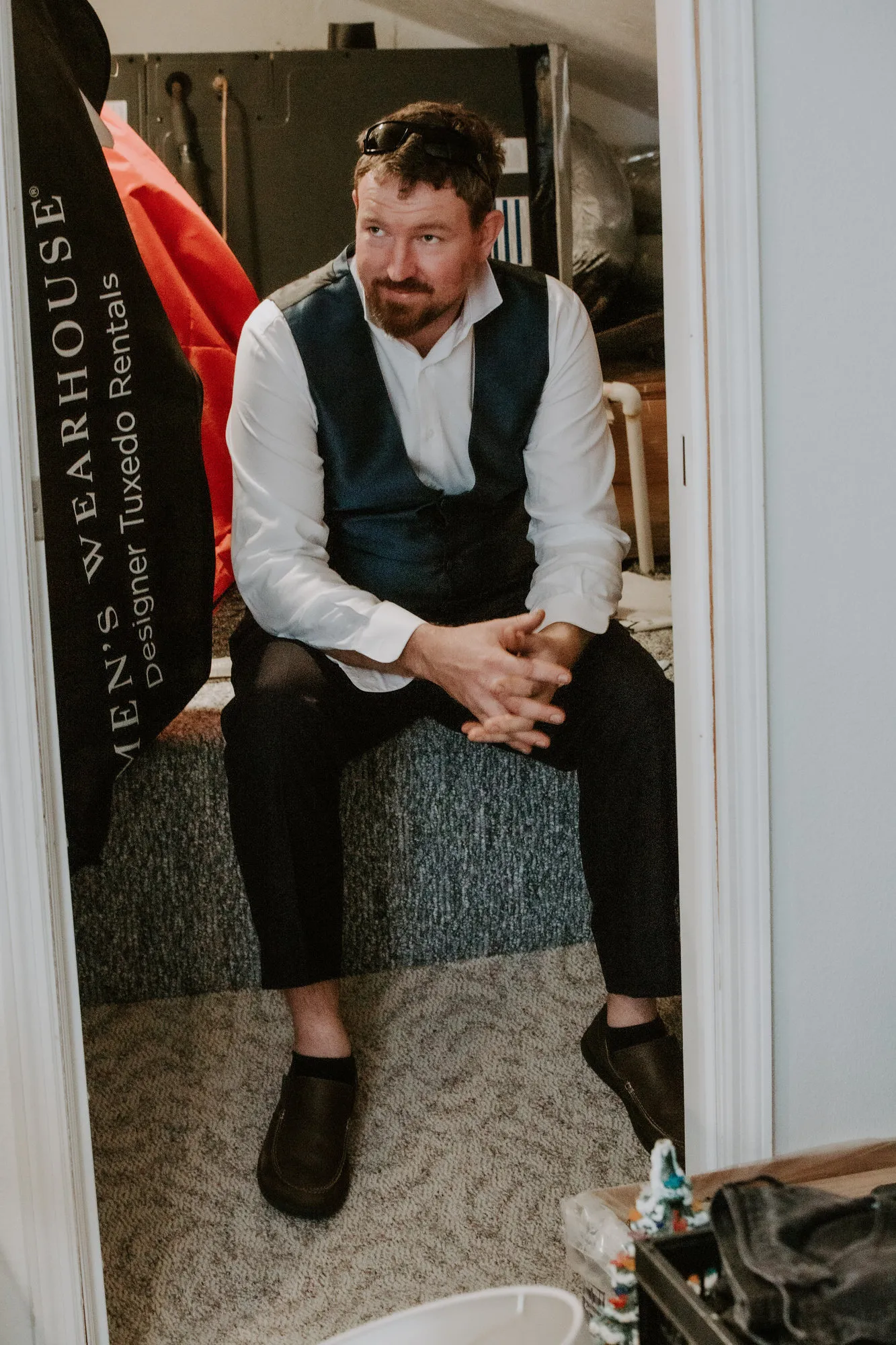 Groom in a vest sitting in a doorway, smiling