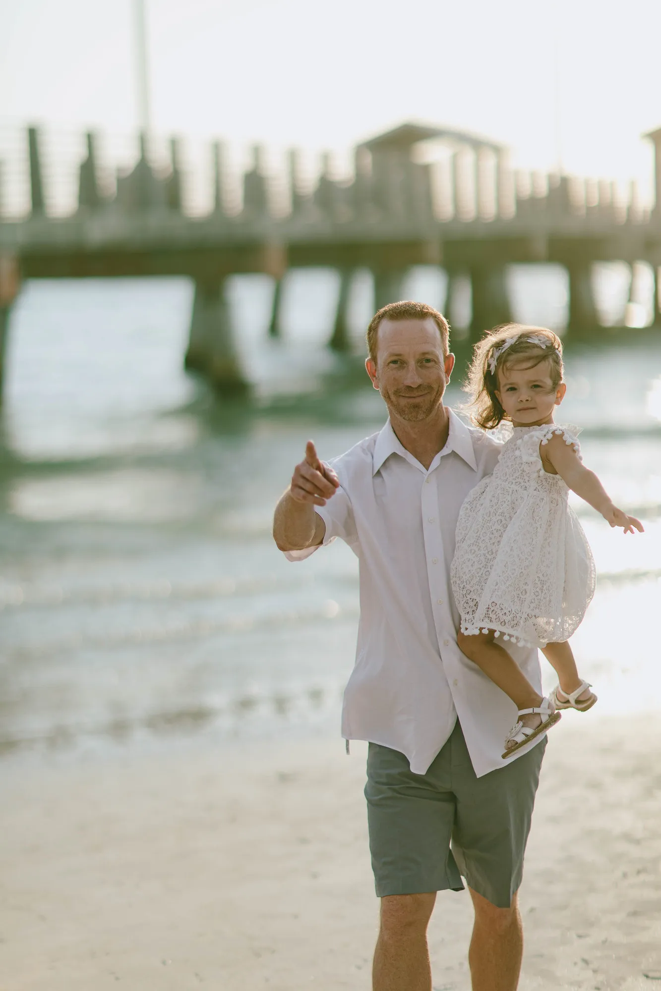 Father carrying his daughter on his hip and pointing at the camera