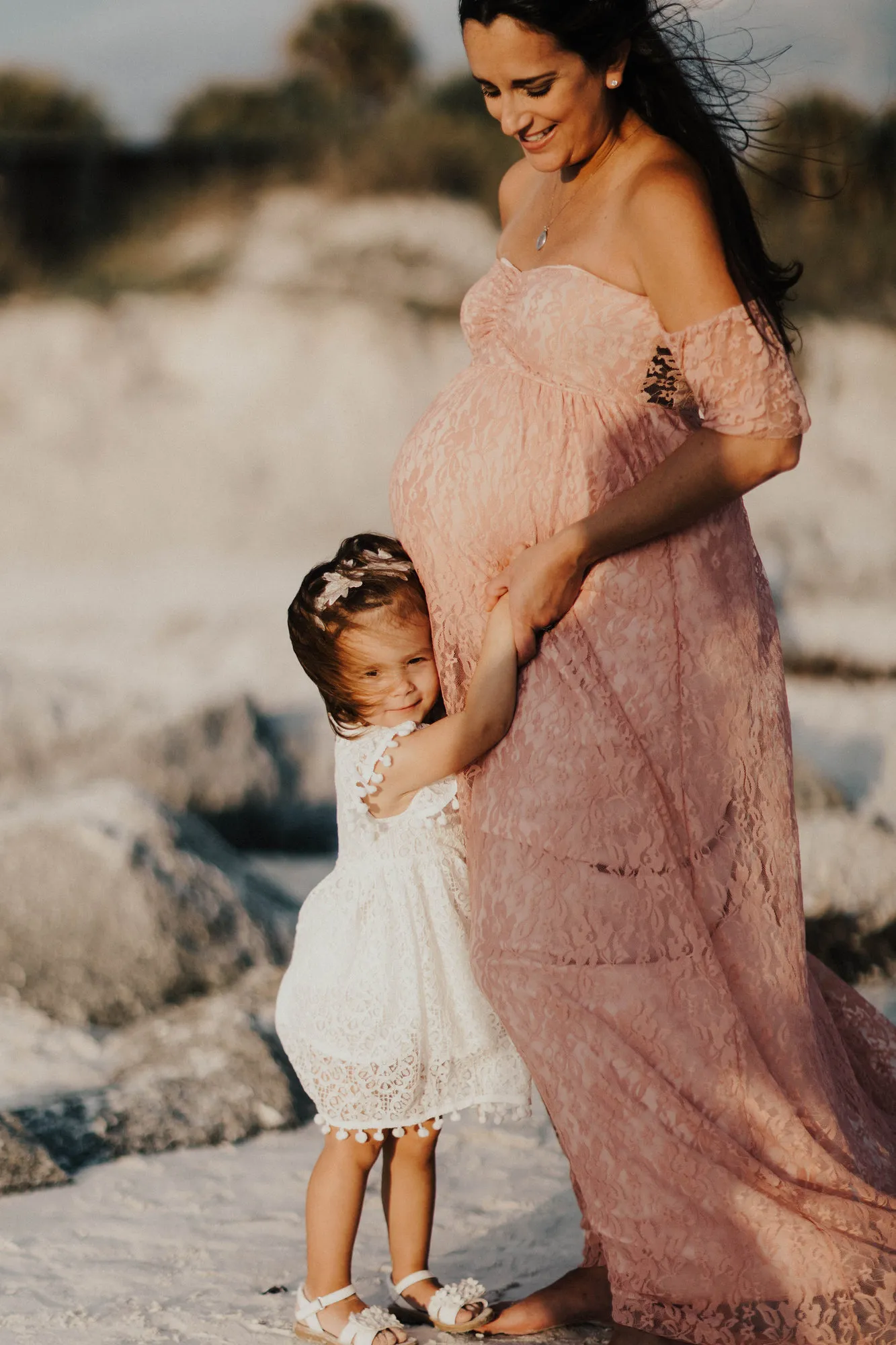 Toddler hugging her mother's bump beside the rocks