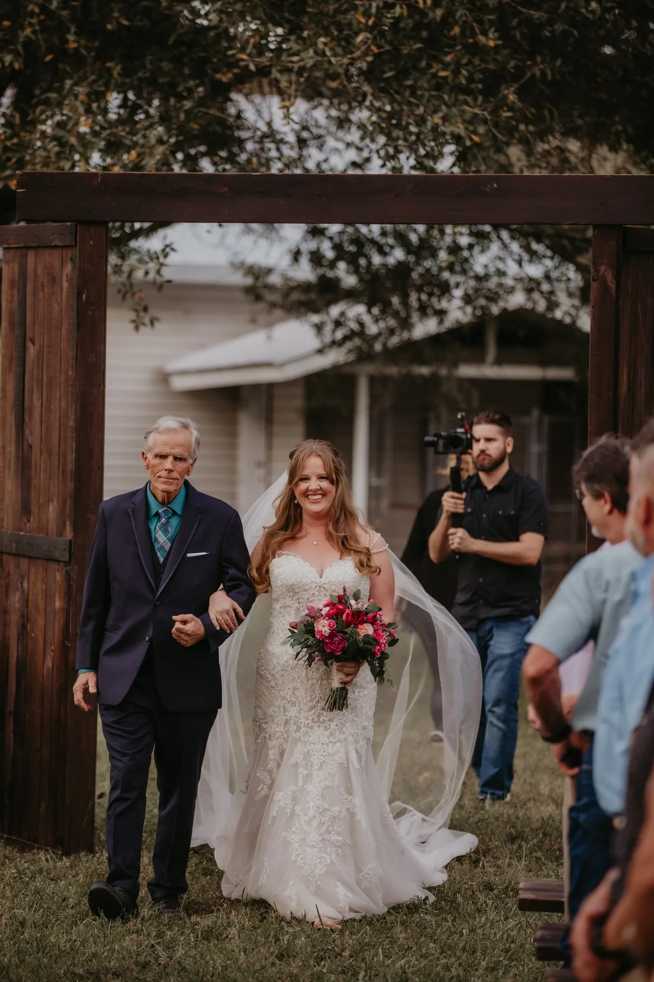Bride smiling as she walks down the aisle on an older man's arm