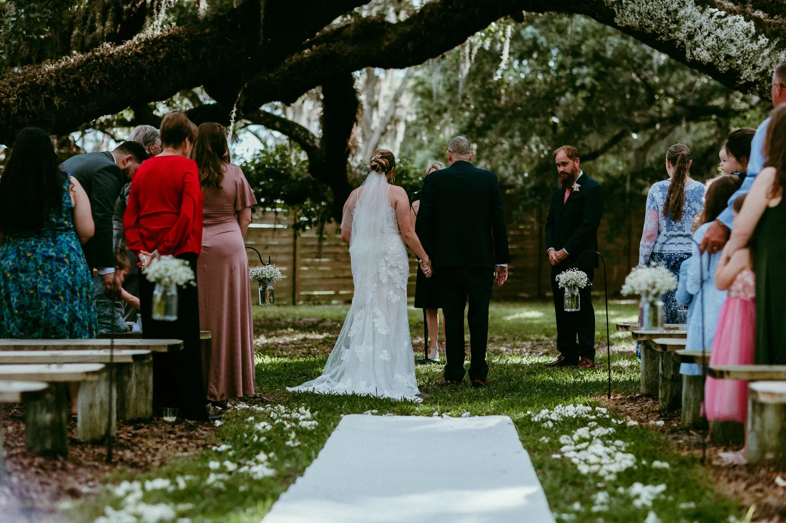Ceremony beneath spreading oak branches, seen from the end of the aisle