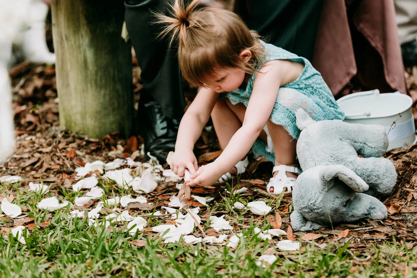 Toddler flower girl crouching to pick up petals