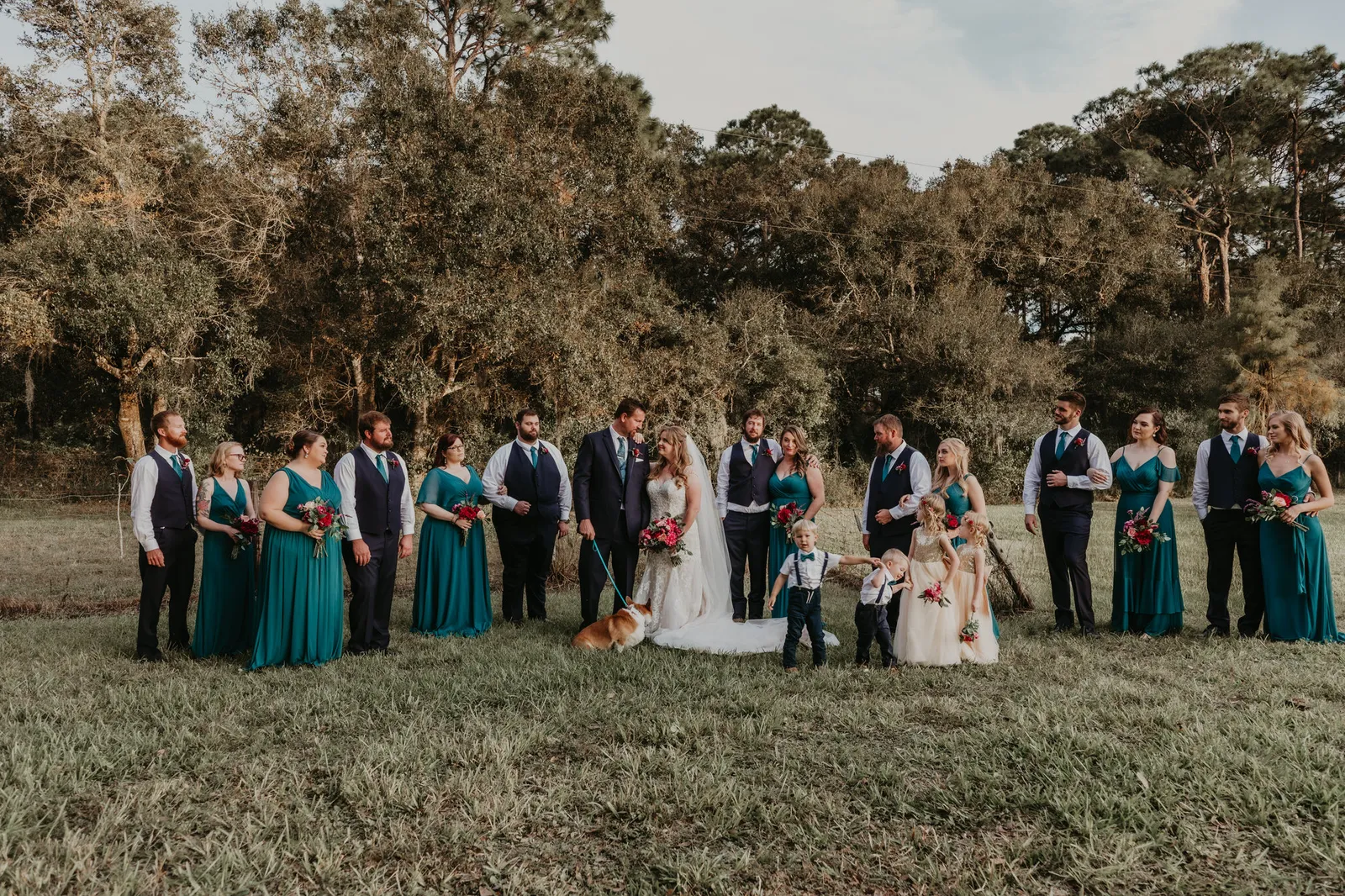 Wedding party lined up in a field, bridesmaids in teal